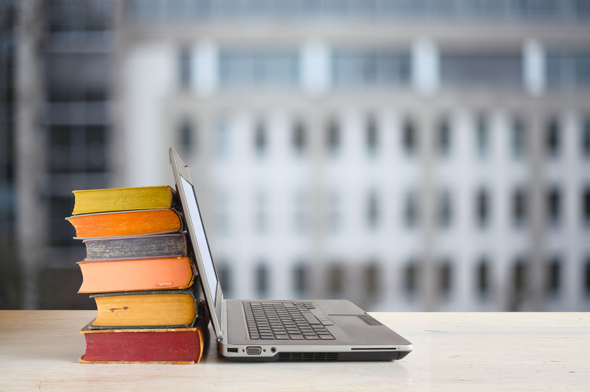 Laptop computer and stack of books ,blurred office building as background.Beat the clock,office work,education concept.Free copy space.